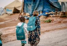 photograph of children with blue backpacks walking